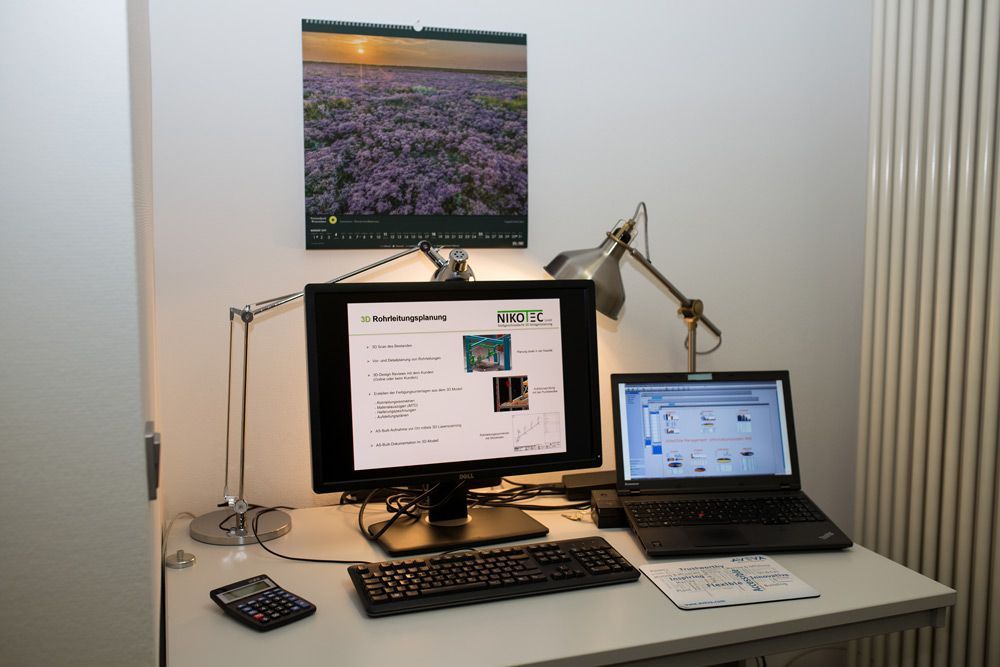 Desktop-Arbeitsplatz mit zwei Monitoren, Laptop, Tastatur und Schreibtischlampe auf einem weißen Schreibtisch.