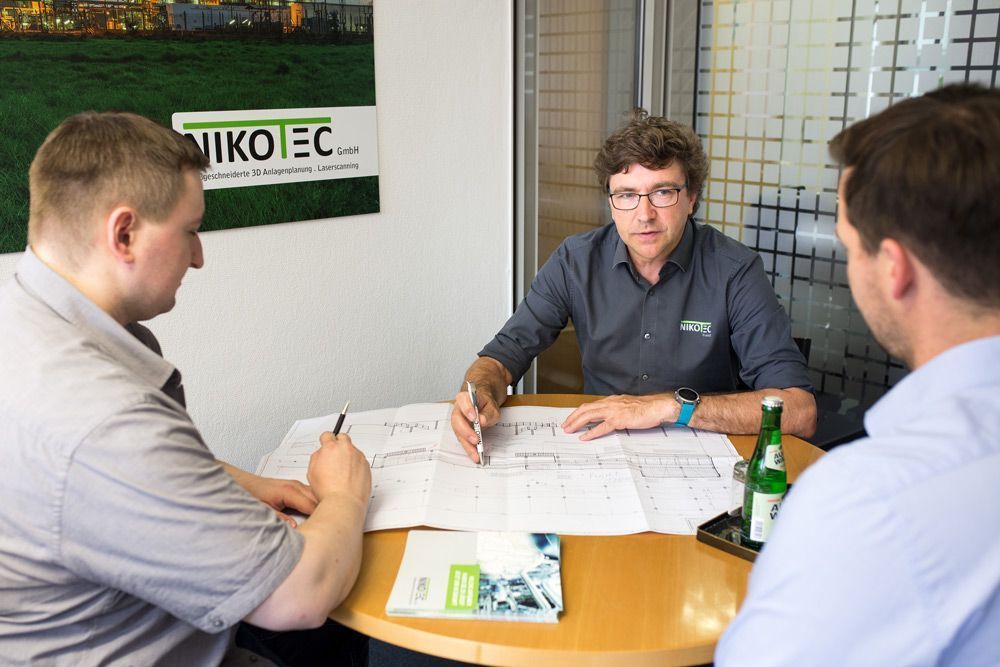 Drei Personen sitzen an einem runden Tisch in einem Büro und besprechen Dokumente.