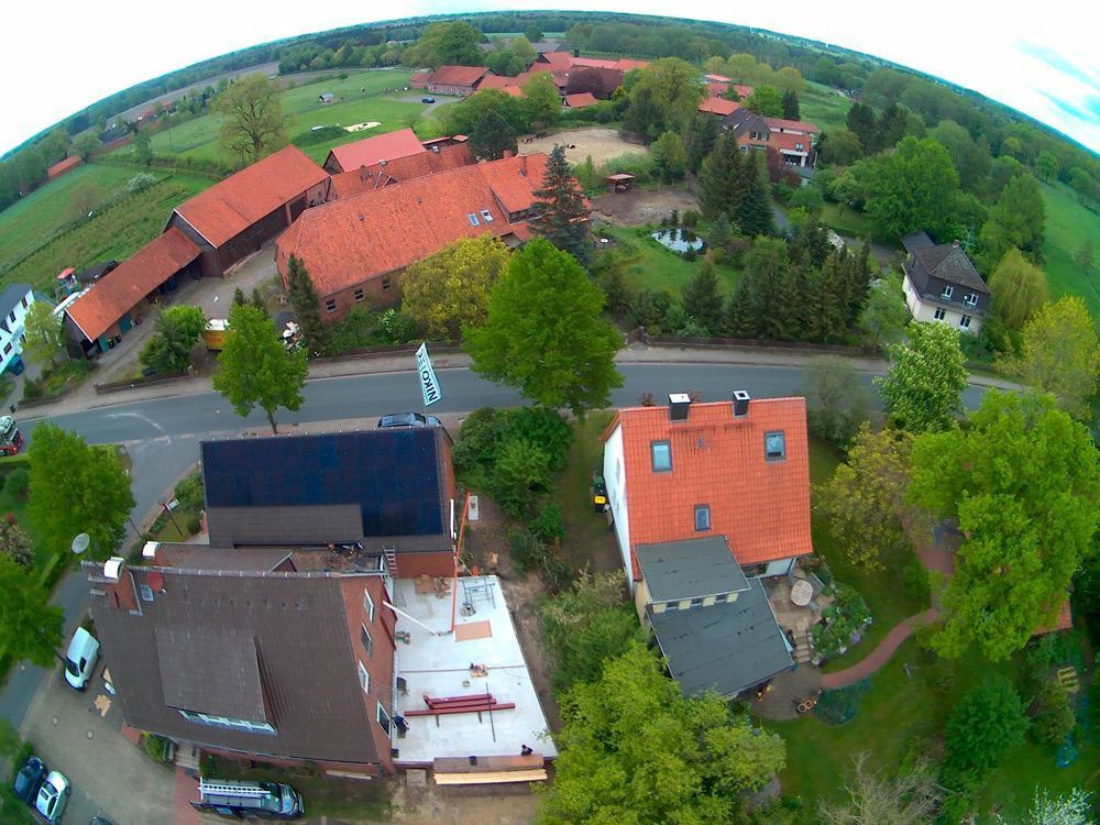 Luftaufnahme von Häusern mit roten Dächern entlang einer Straße, umgeben von grünen Bäumen und Feldern