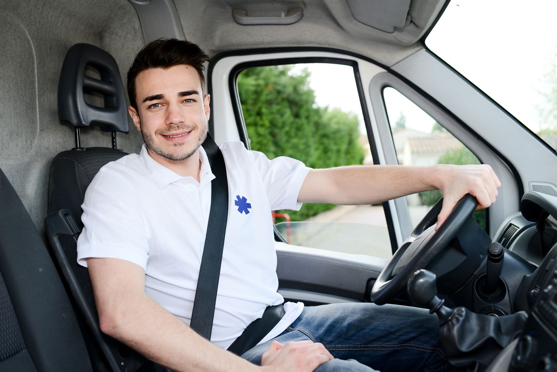 Un jeune homme conduit une ambulance. Il est vêtu d'un tee-shirt blanc avec une étoile de vie brodée.