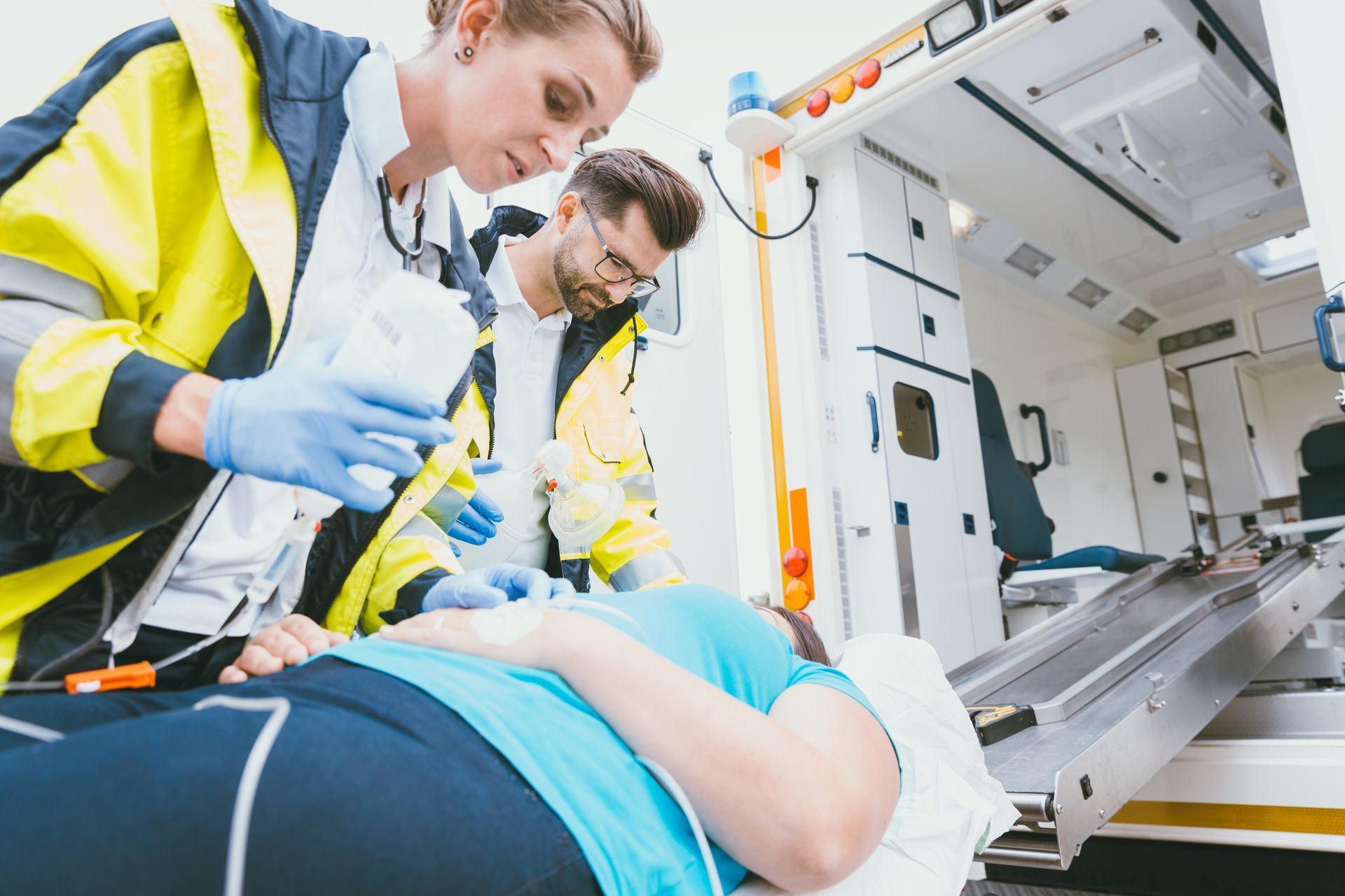Des ambulanciers soignent un patient sur une civière à l'aide d'une perfusion et d'un masque à oxygène.