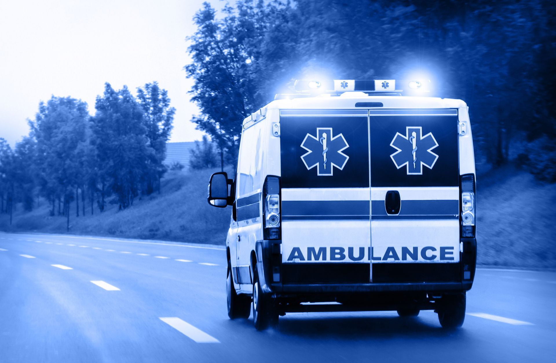 Ambulance bleue circulant sur une route, gyrophares allumés et étoiles de vie à l'arrière.