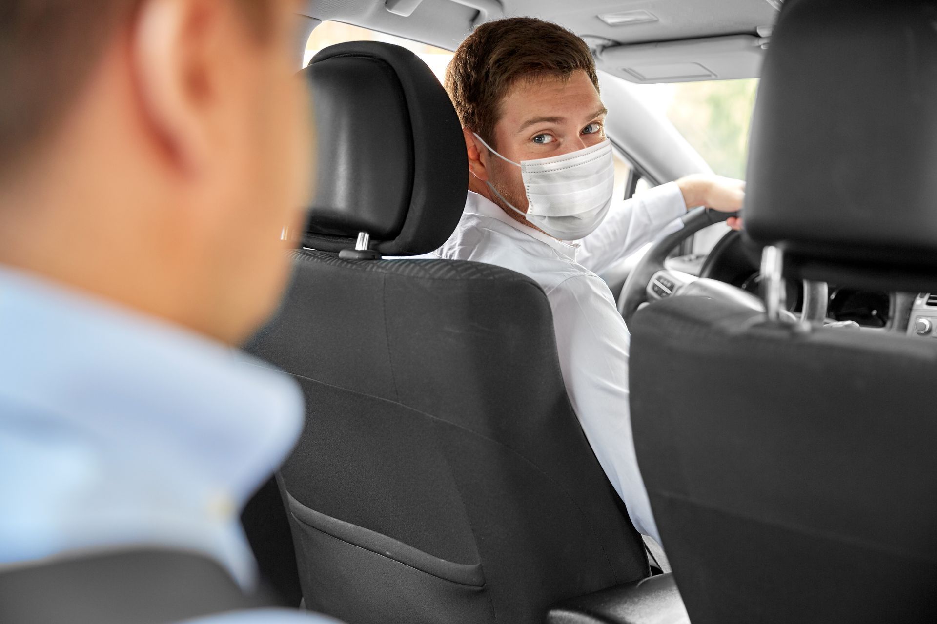 Un conducteur portant un masque blanc se retourne pour parler au passager installé sur le siège arrière.
