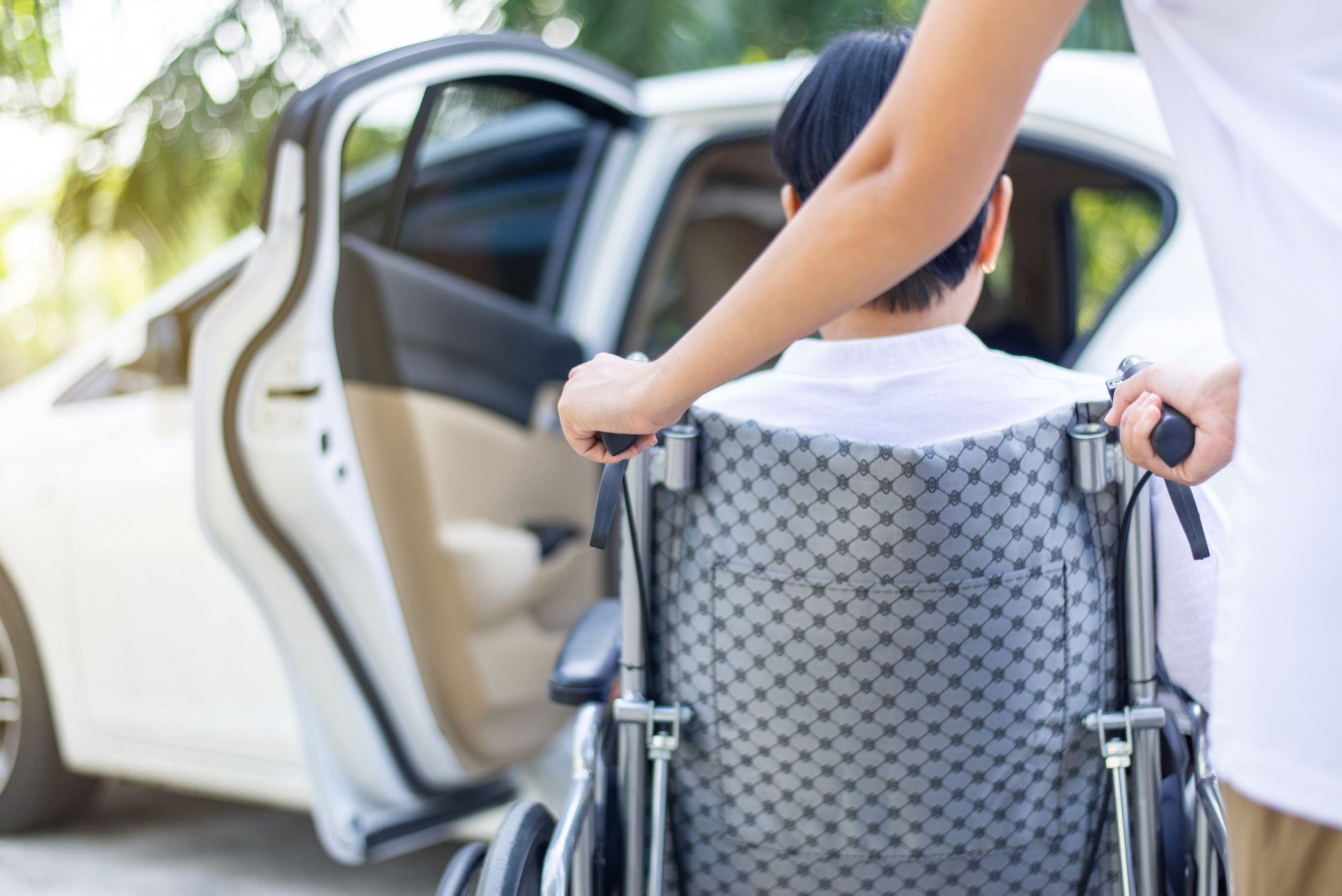 Une personne pousse une personne en fauteuil roulant vers une portière de voiture blanche ouverte.