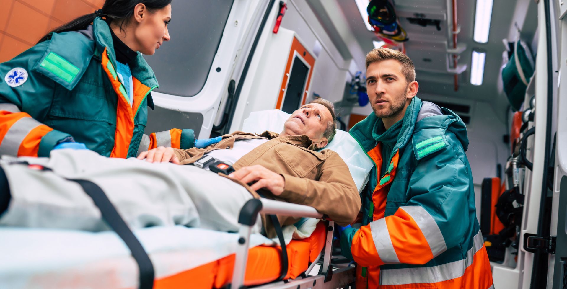 Des ambulanciers en uniforme orange et turquoise stabilisent un homme blessé sur une civière.