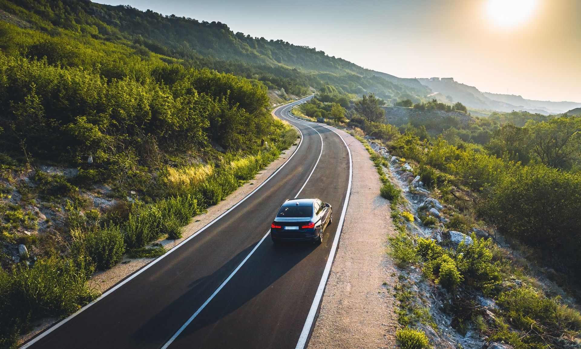 Voiture sur une route sinueuse à travers des collines verdoyantes au lever du soleil.
