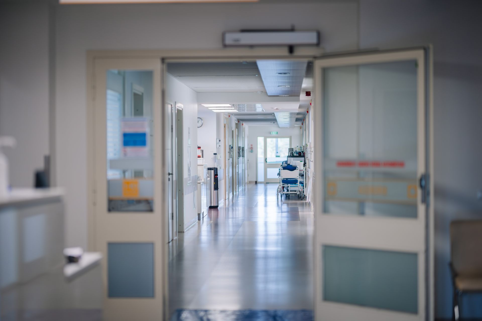 Couloir d'hôpital ouvert avec des portes doubles et un brancard au loin.