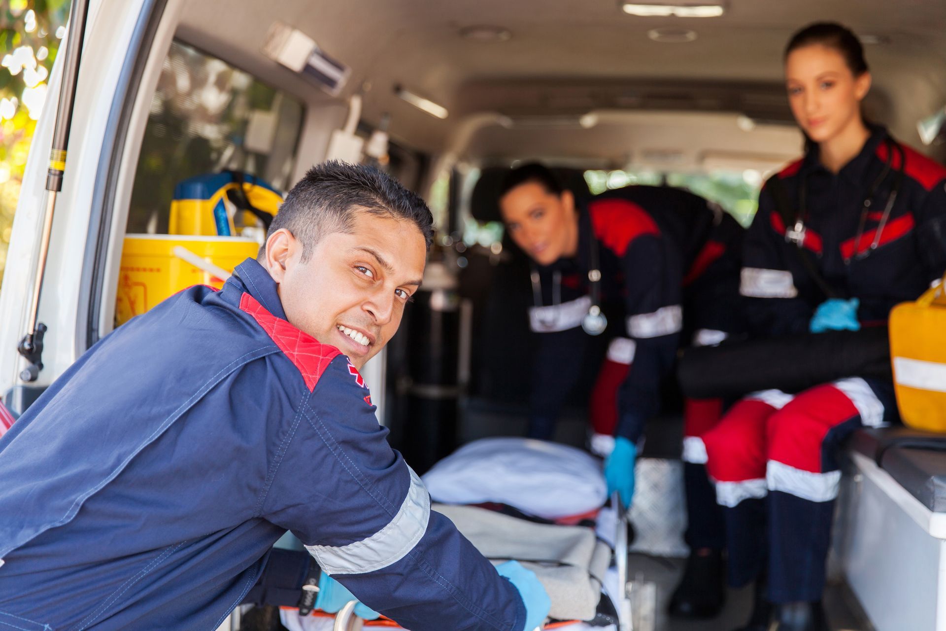 Des ambulanciers préparent une civière et du matériel médical à l'intérieur du véhicule.