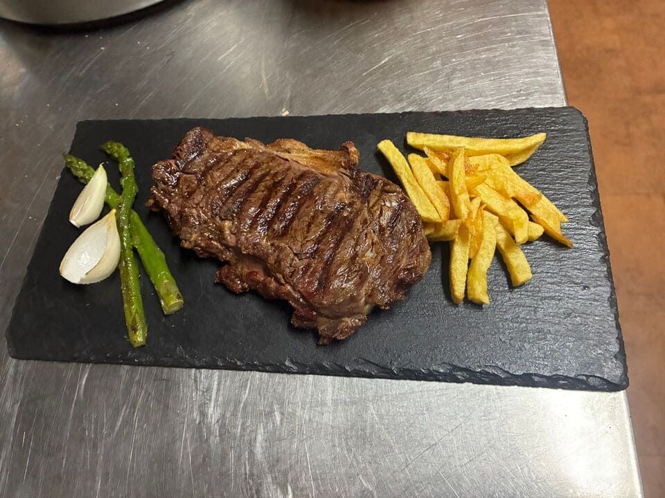 Un trozo de carne  y patatas fritas en un plato negro