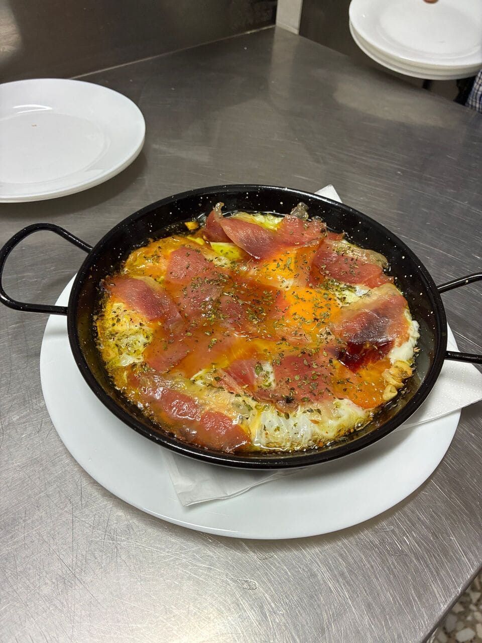 Una sartén con huevos rotos está colocada en un plato blanco sobre una mesa.