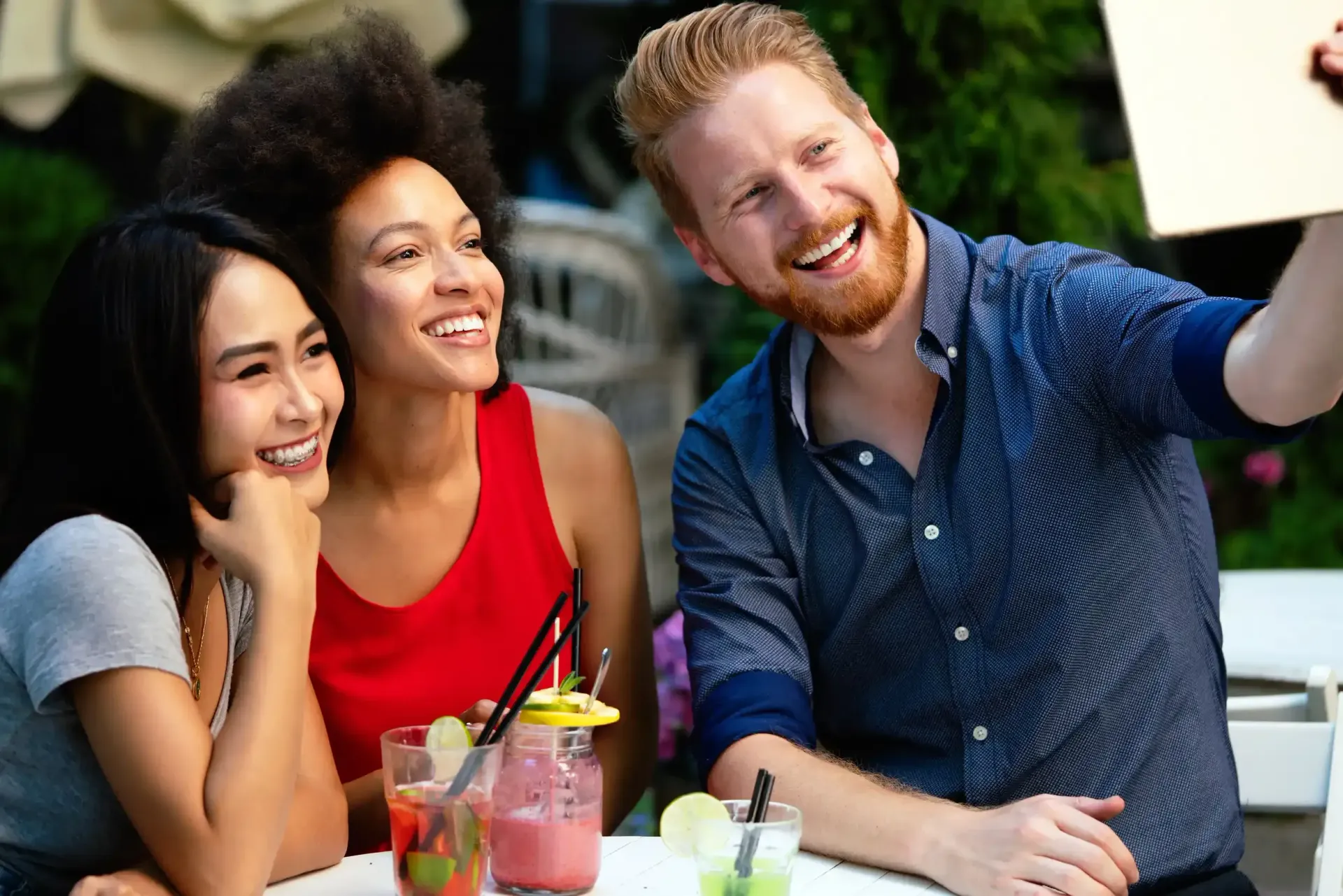 Un hombre se toma una selfie con dos mujeres mientras está sentado en una mesa con bebidas.