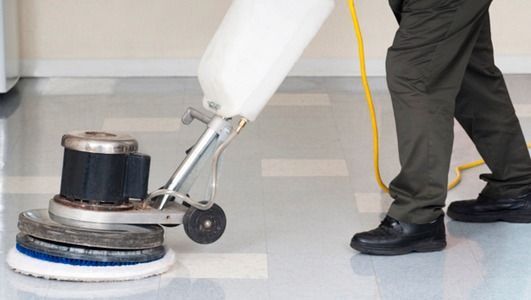 Persona utilizando una pulidora de suelos para limpiar un suelo brillante de color claro. Se ve el cable de alimentación amarillo.
