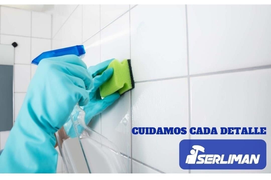 Persona con guantes azules limpiando una pared de azulejos blancos con una botella con pulverizador y una esponja.