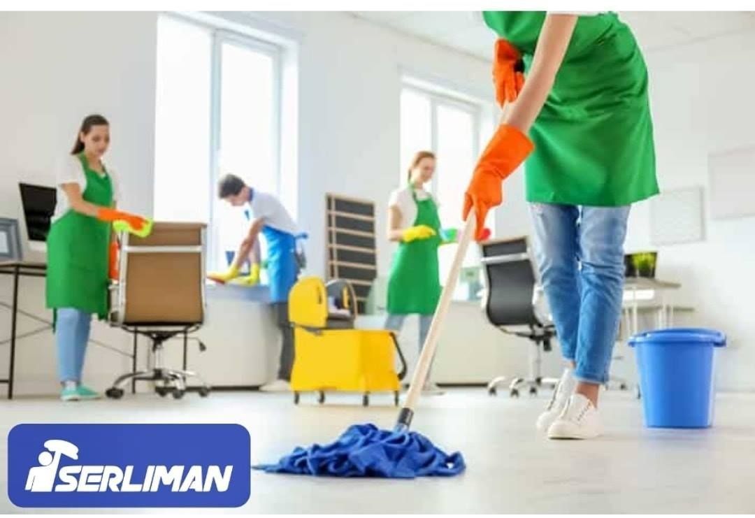 Personal de limpieza de oficinas fregando el suelo y limpiando las superficies. Cuatro personas con delantales verdes y guantes naranjas.