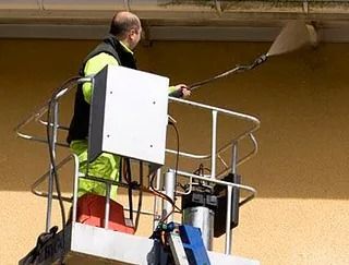 Persona en la plataforma elevadora limpiando el exterior del edificio con una manguera de alta presión.