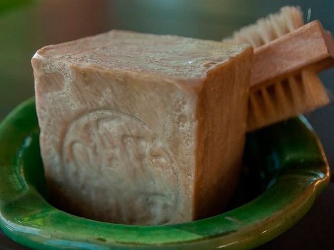 Jabón marrón en pastilla en un plato de cerámica verde con un pequeño cepillo de madera.