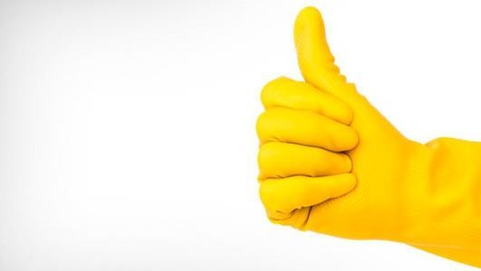 Mano enguantada de amarillo haciendo el gesto de aprobación con el pulgar sobre fondo blanco.