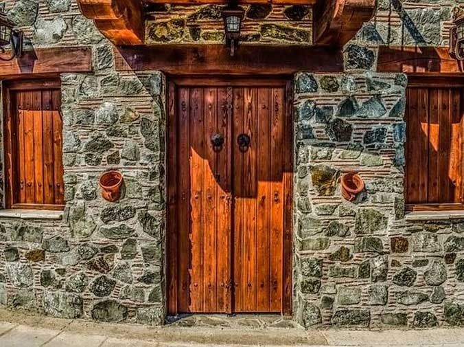 Puerta de madera con paredes de piedra y contraventanas de madera, con una linterna sobre la puerta.