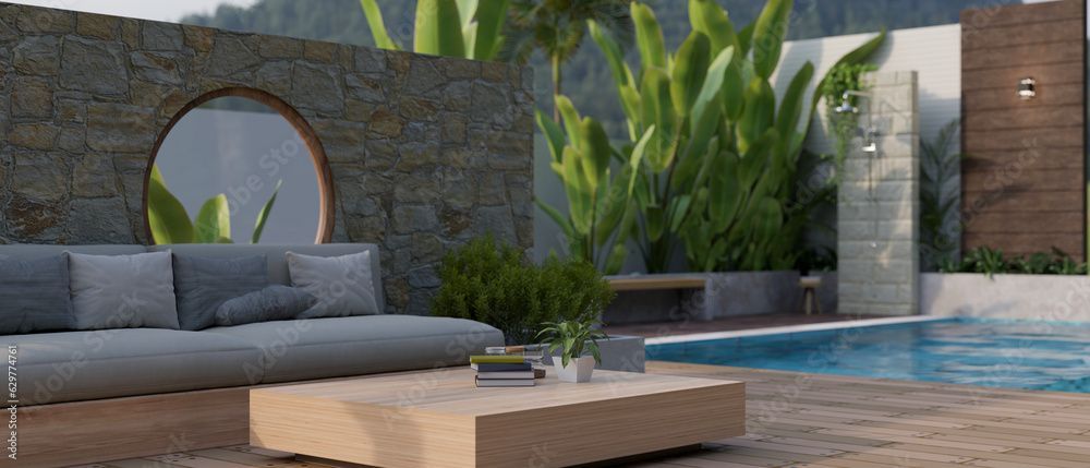 Moderne Terrasse mit grauem Sofa, Holztisch, üppigen Pflanzen und einem Pool neben einer Steinmauer.