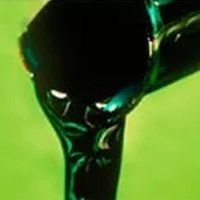 Un primer plano de una gota de líquido negro sobre una superficie verde.