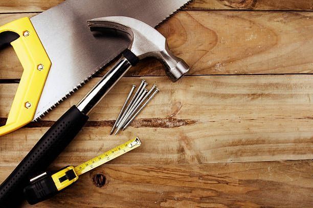 Un martillo, una sierra, una cinta métrica y clavos están sobre una mesa de madera.