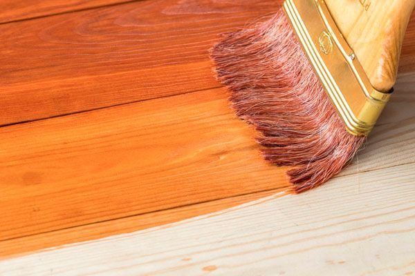 Un primer plano de un pincel pintando un piso de madera.
