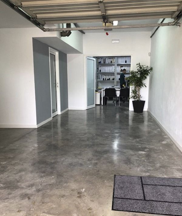 Un garaje luminoso con suelos de hormigón pulido, una pared decorativa de color gris y un espacio de oficina en la parte trasera con estanterías y escritorios.
