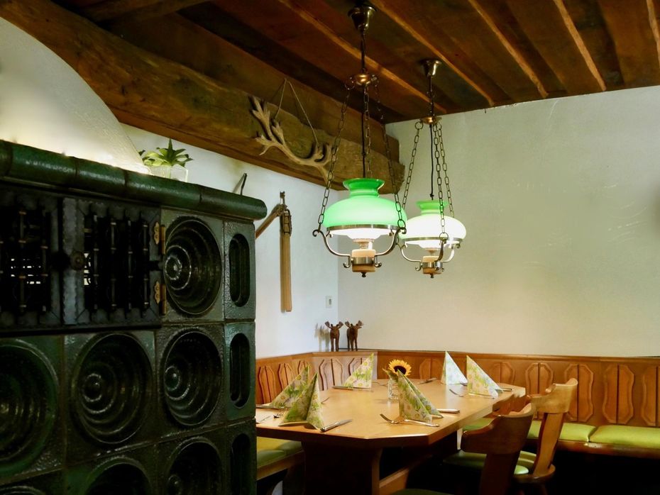 Gemütliches Restaurantinterieur mit Holzbalken, grünen Lampen und einer Ecknische mit gedecktem Tisch.