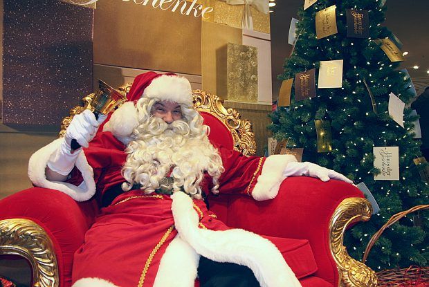 Weihnachtsmann mit Glocke sitzt auf Rotem Sessel