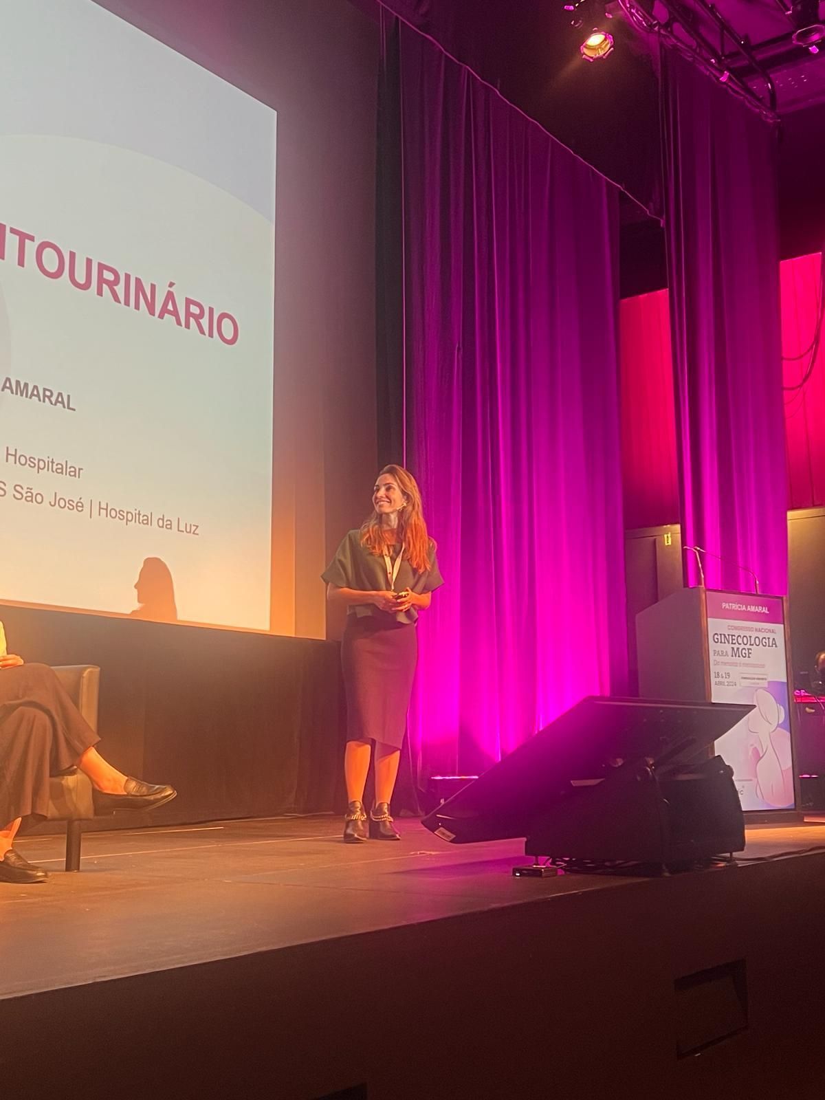 Mulher no palco apresentando em um evento. Iluminação, palco e cortinas roxas.