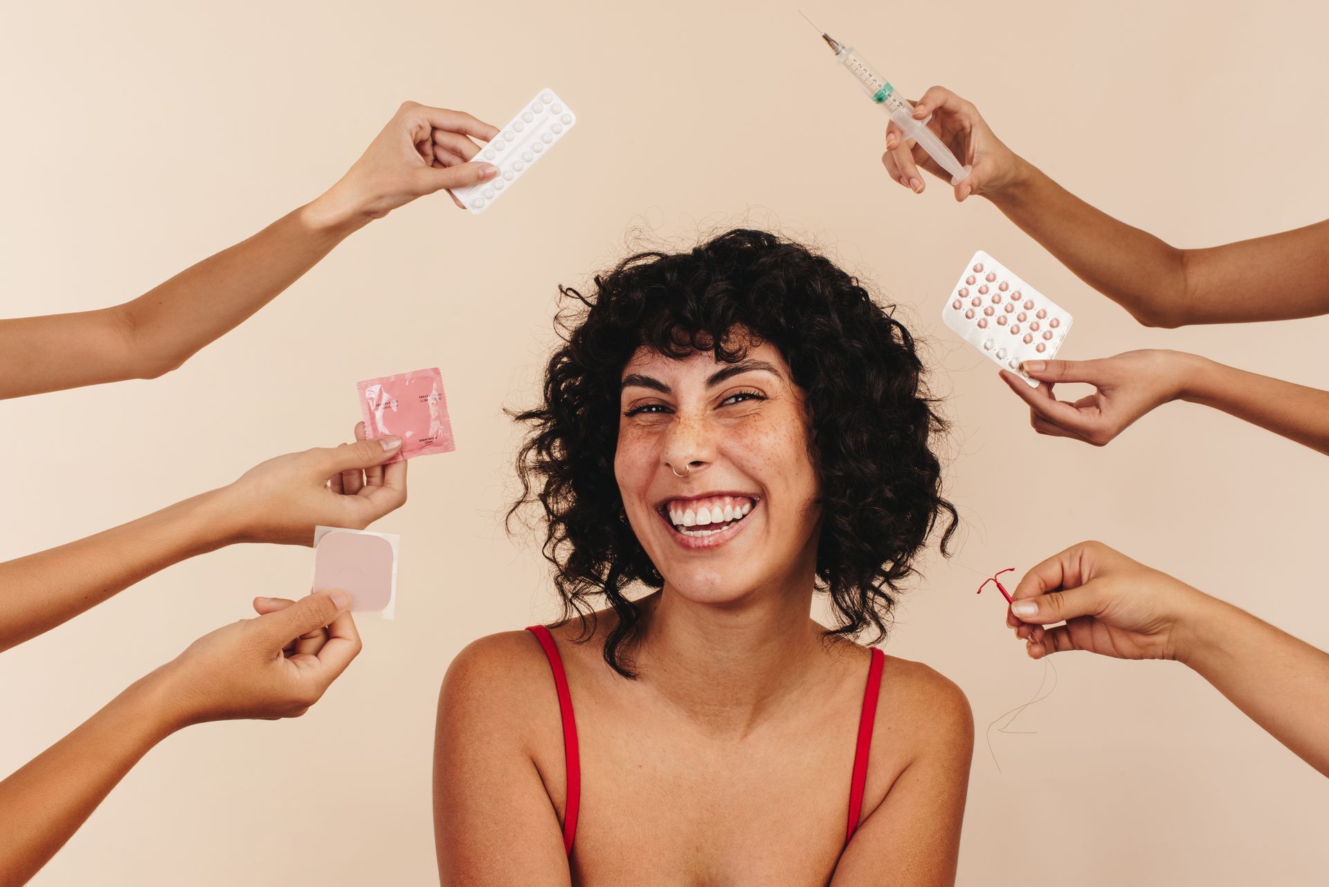 Mulher sorridente, rodeada por mãos que seguram vários métodos contraceptivos, contra um fundo claro.
