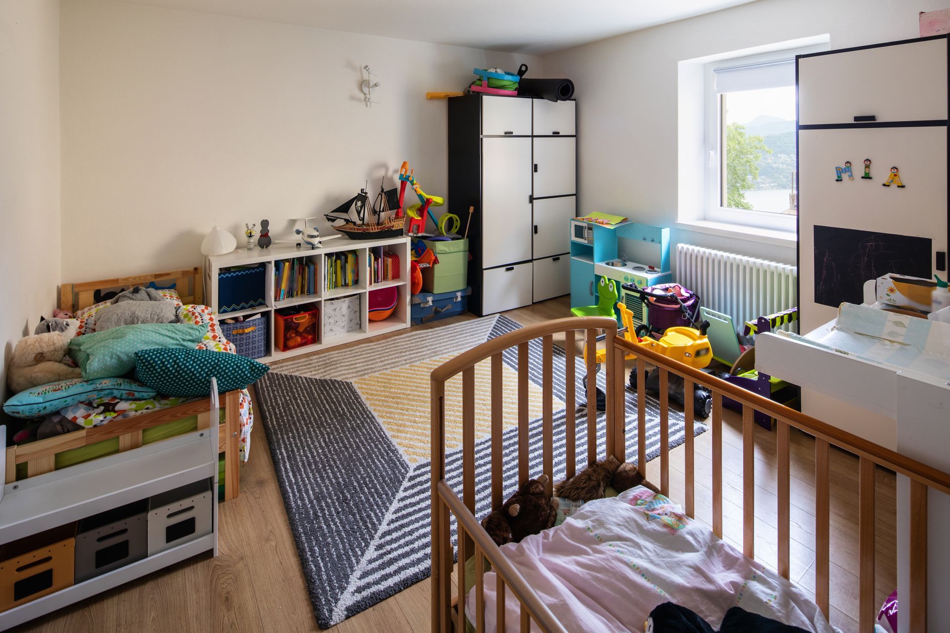 Chambre d'enfant avec lit superposé, jouets, bacs de rangement et lumière naturelle abondante.