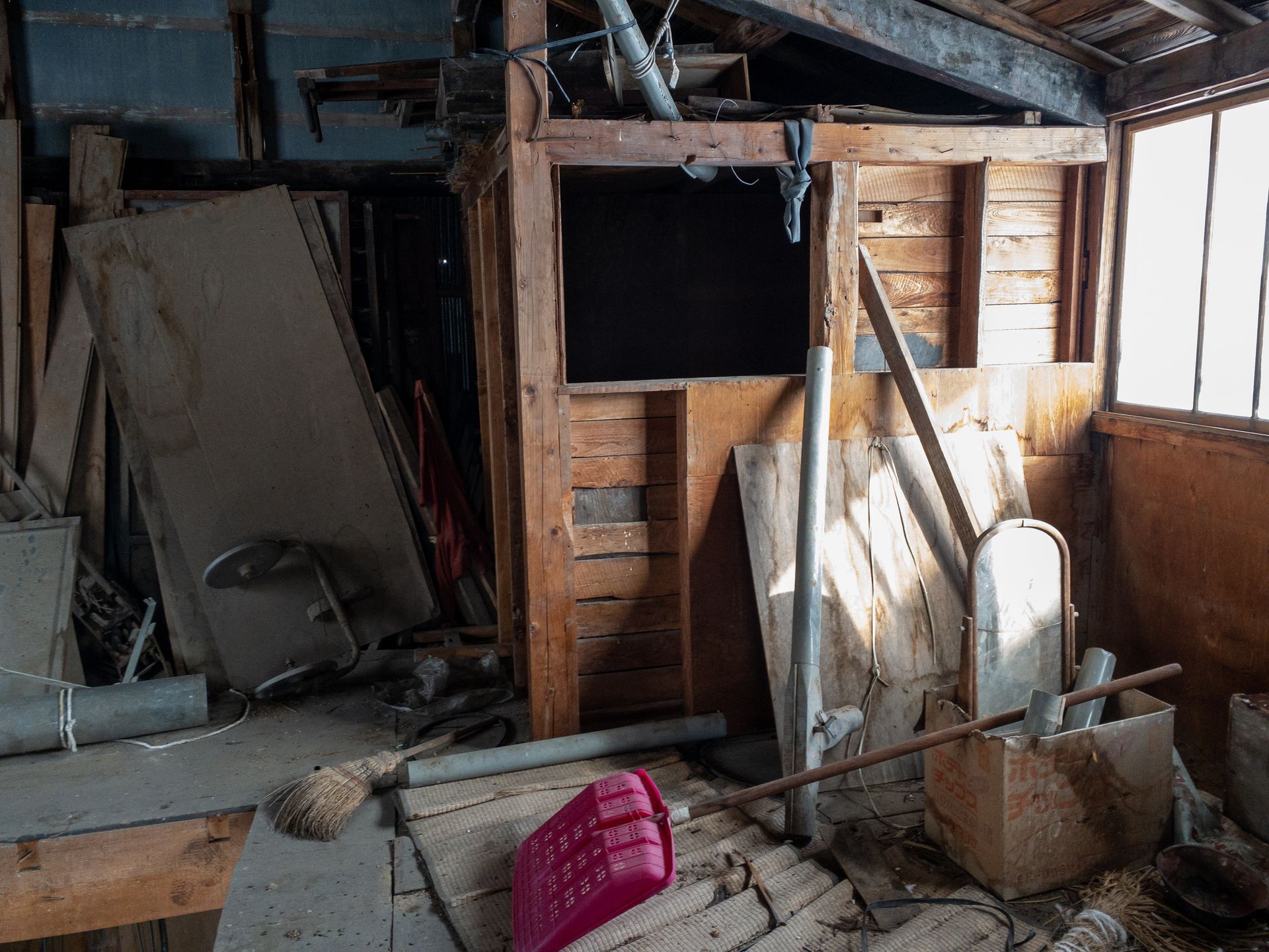 Intérieur d'un hangar en bois abandonné, jonché de débris, d'outils et d'ouvertures de fenêtres baignées de soleil.