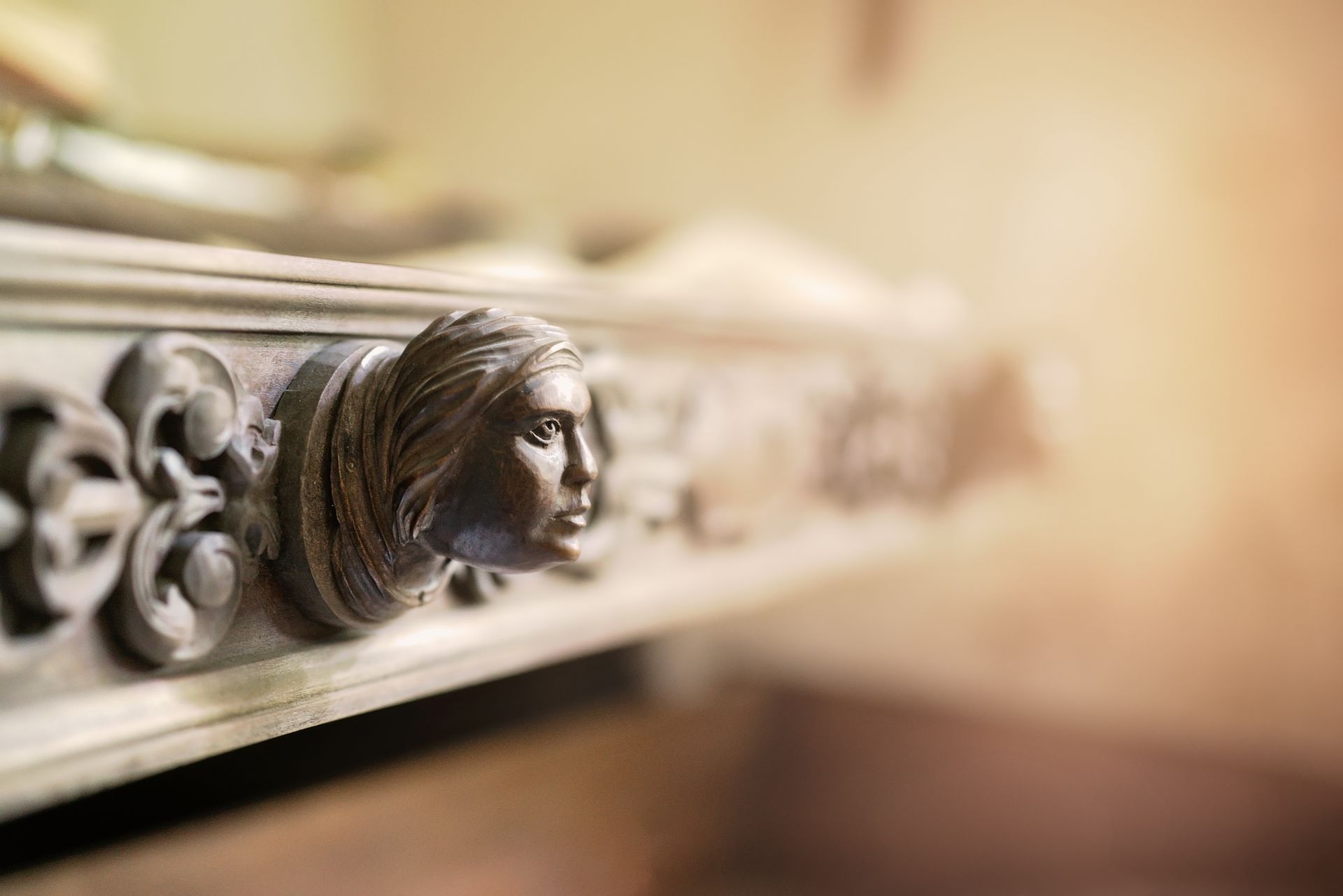 Gros plan sur un visage en bois sculpté et orné, sur une moulure architecturale décorative.