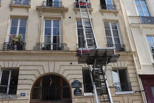 Façade d'immeuble beige dans une rue de la ville, avec un ascenseur à grande échelle desservant les étages supérieurs.