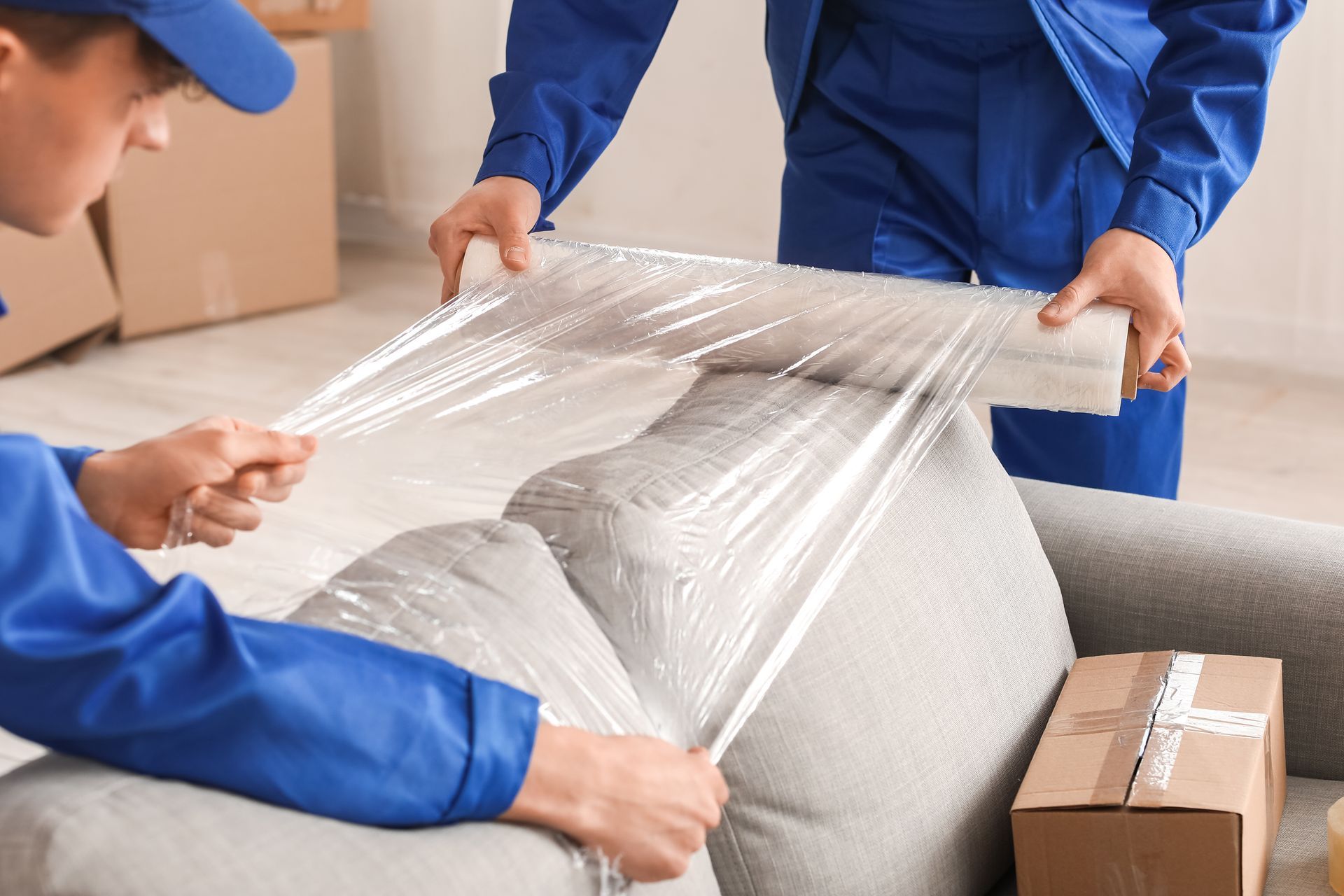 Des ouvriers en uniforme bleu emballent des meubles avec du film plastique transparent dans un camion de déménagement.