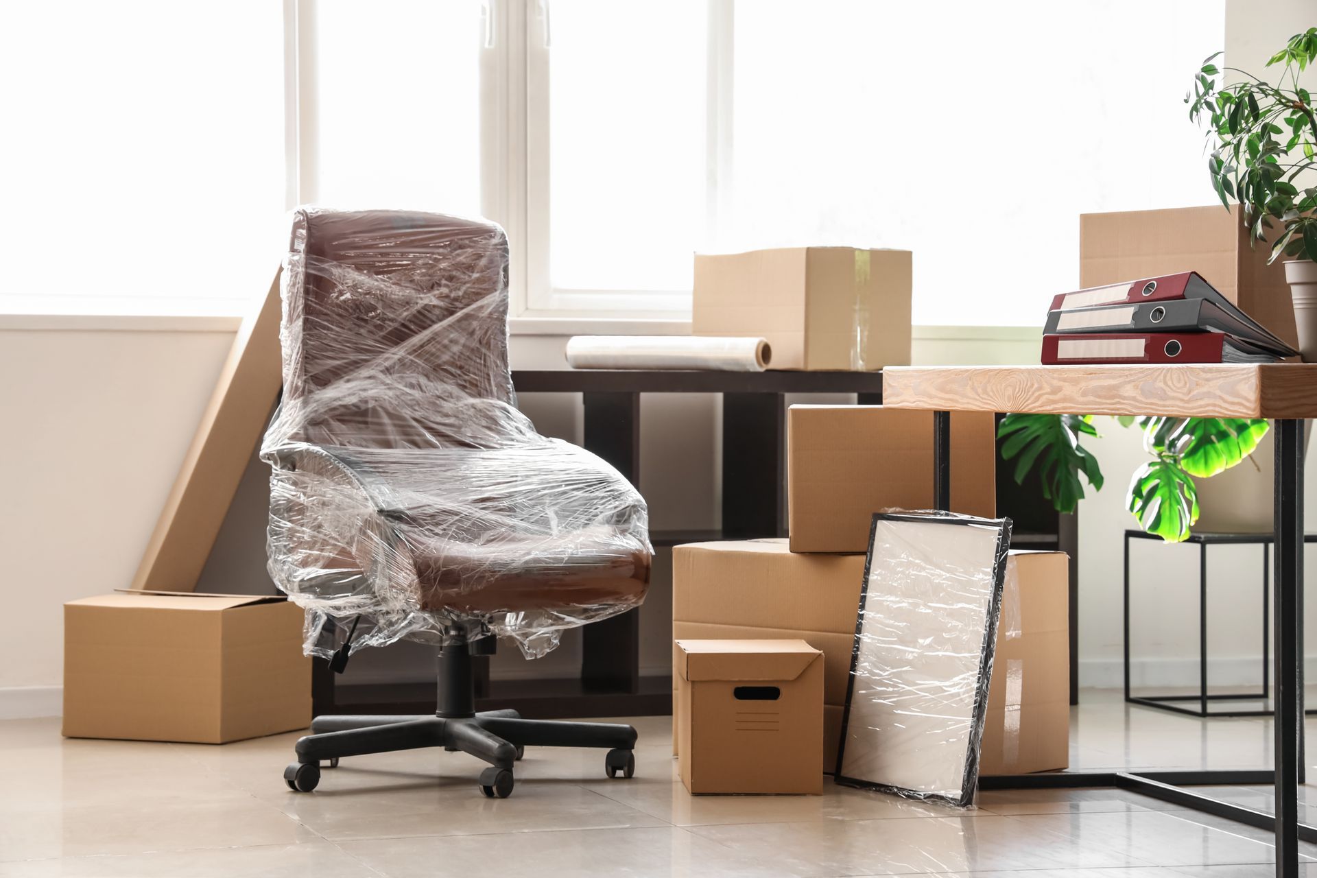 Des cartons de déménagement et une chaise de bureau emballée dans une pièce lumineuse.