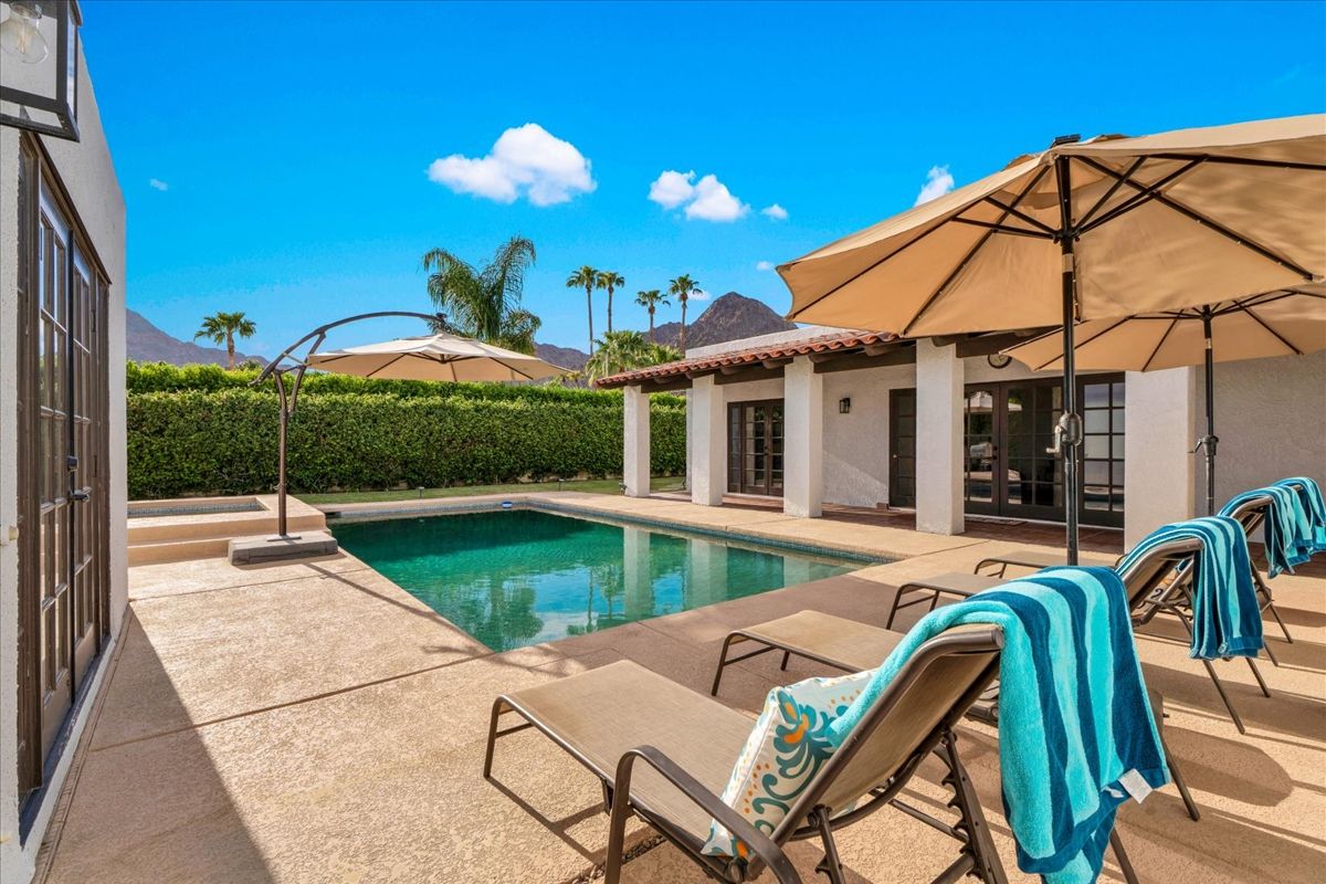 pool with lounge chairs and umbrella outside of spanish style home