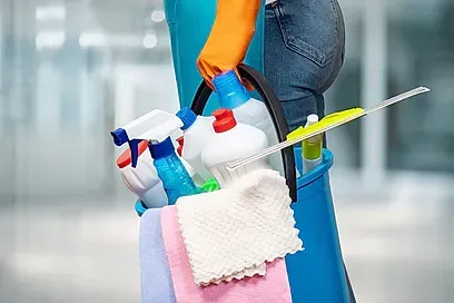 Una mujer lleva un balde lleno de productos de limpieza.