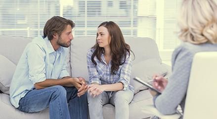 Dos personas hablando con un terapeuta en una consulta luminosa, sentadas en un sofá.