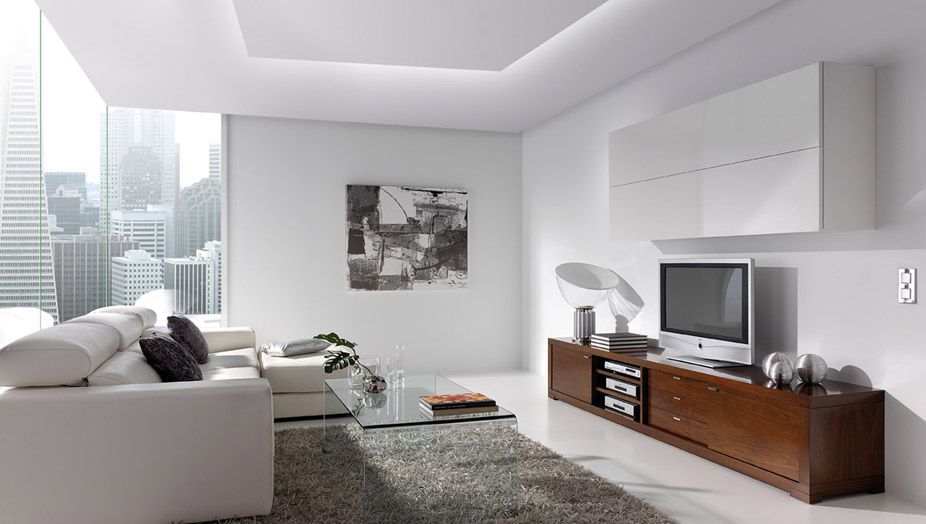 Salón moderno con paredes blancas, sofá seccional y mueble de televisión con televisor, con vistas a la ciudad.