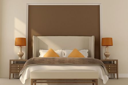 Dormitorio con cama, mesitas de noche, lámparas y un detalle marrón en la pared.