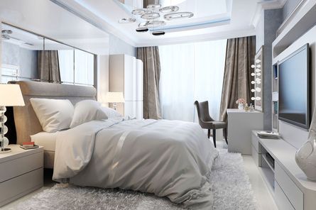 Dormitorio moderno con cama grande, pared espejada y mueble para la televisión. Paleta de colores en tonos grises suaves y blancos.