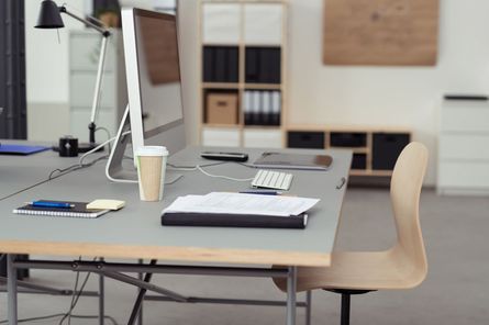Escritorio con ordenador, taza de café, papeles y silla.
