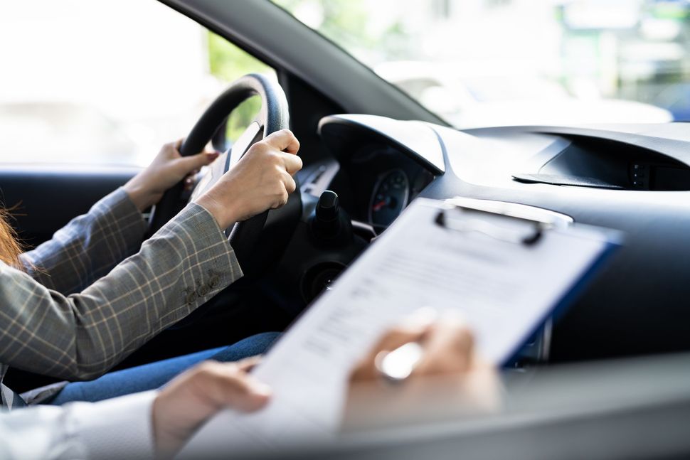 Eine Frau fährt Auto, während eine andere Person ein Klemmbrett hält.