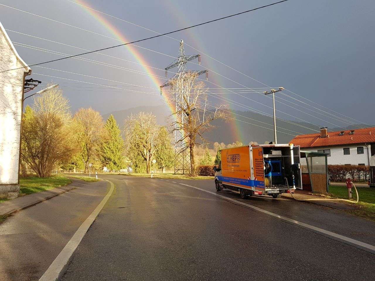 Kanalreinigung - Eine Straße mit einem Hepp Fahrzeug und darüber ein doppelter Regenbogen am Himmel