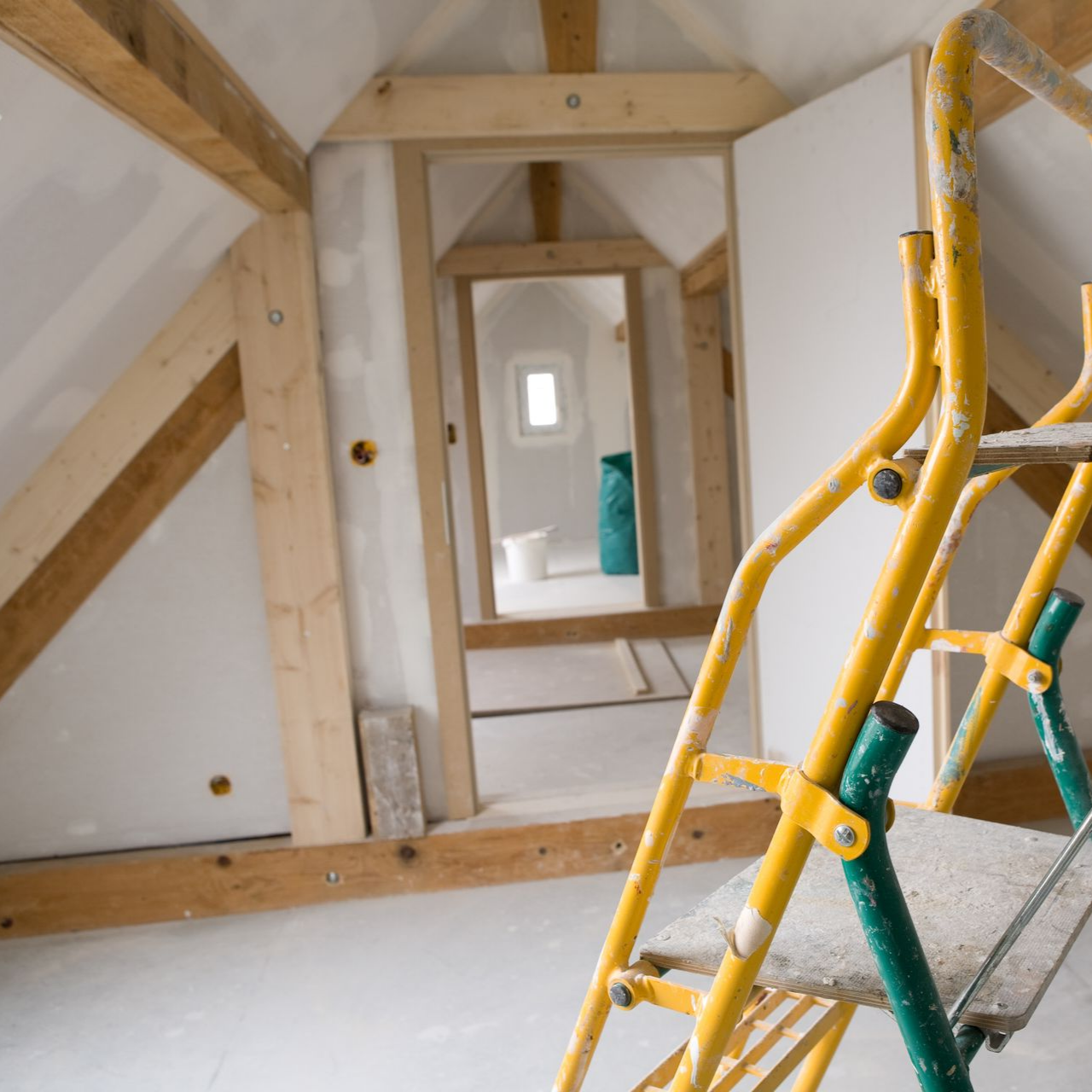 Intérieur d'un grenier non aménagé avec une échelle jaune. Poutres en bois et cloisons sèches apparentes.