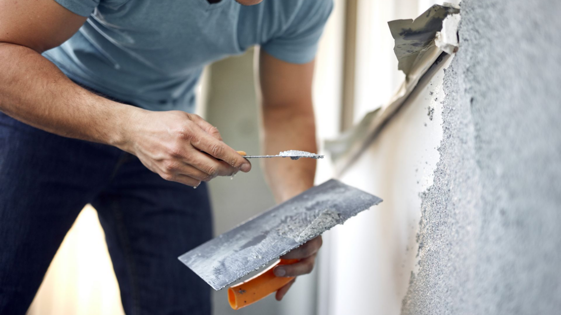 Une personne utilise une truelle pour gratter le plâtre qui s'écaille d'un mur.