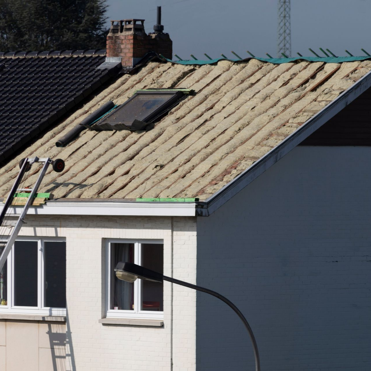 Toiture de maison avec puits de lumière et cheminée, en construction ; extérieur blanc, lampadaire au premier plan.