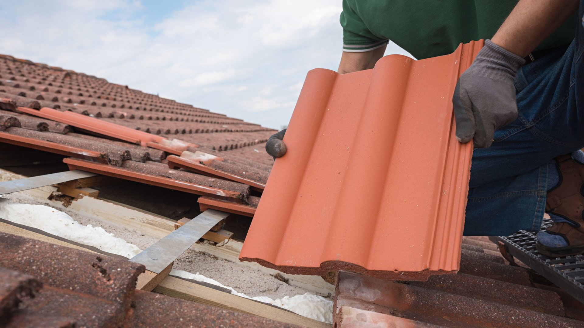 Un couvreur pose des tuiles en terre cuite sur un toit en pente.
